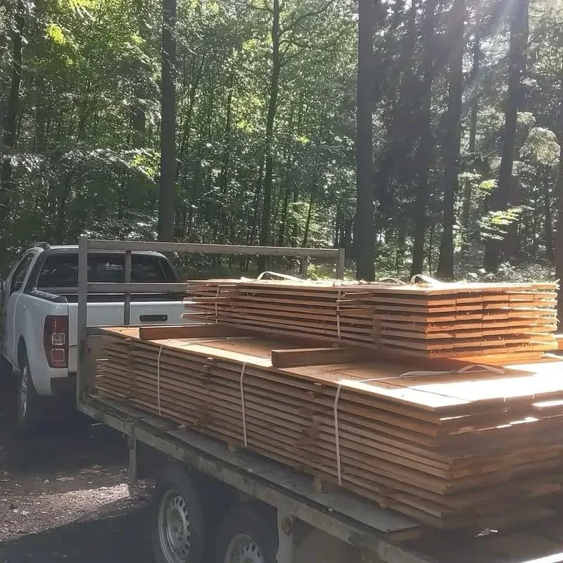 Remorque chargée de piles de bois scié et attelée à un pick-up en forêt