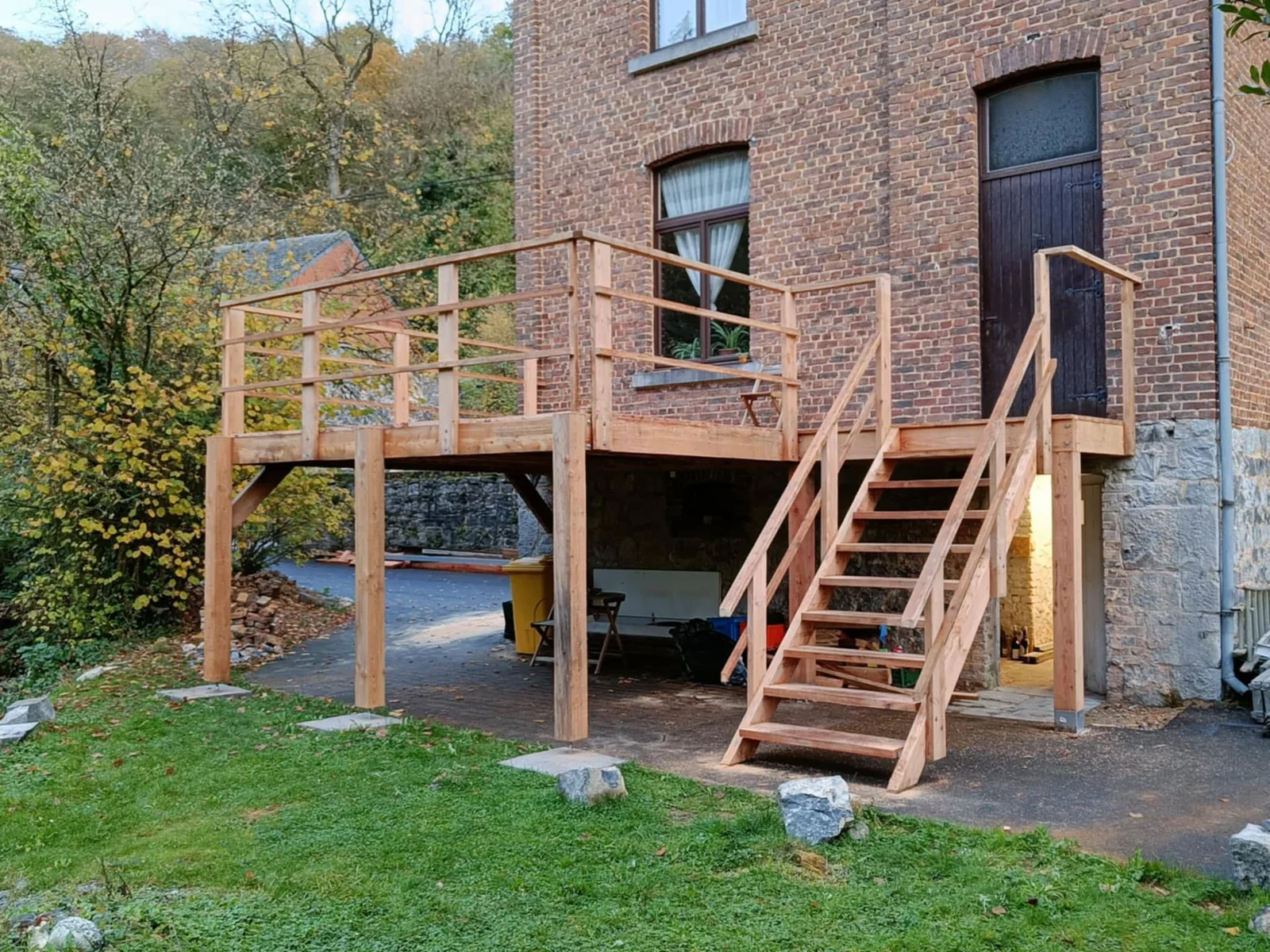Terrasse surélevée en bois réalisée par Adi’Bois, avec son escalier devant une maison en brique en région namuroise
