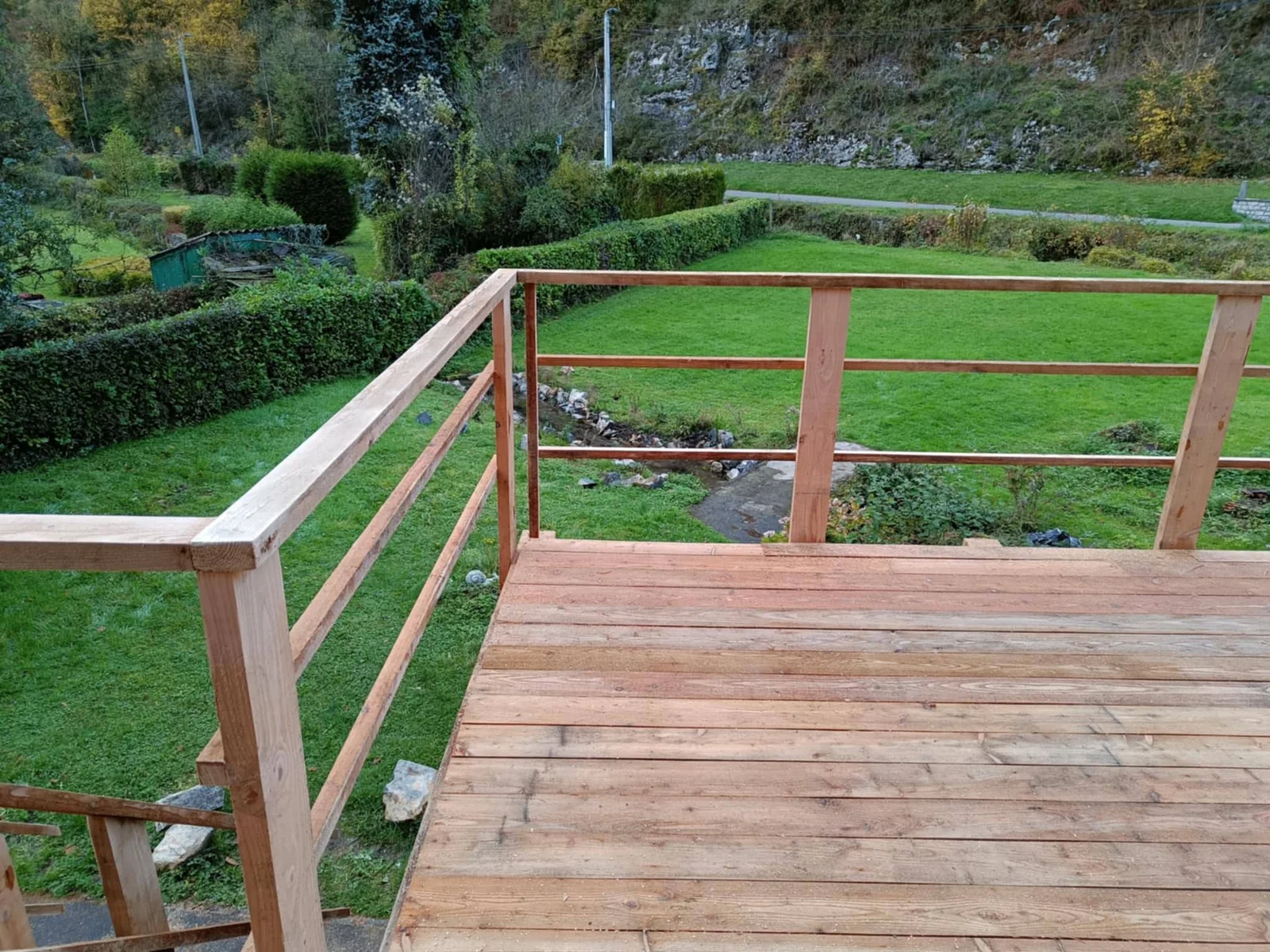 Détail du platelage et de l’angle de la rambarde, avec vue sur le jardin depuis la terrasse Adi’Bois